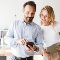 Couple of smiling colleagues looking at mobile phone