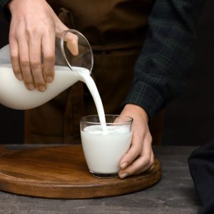 Woman pouring fresh milk from jug into glass on table